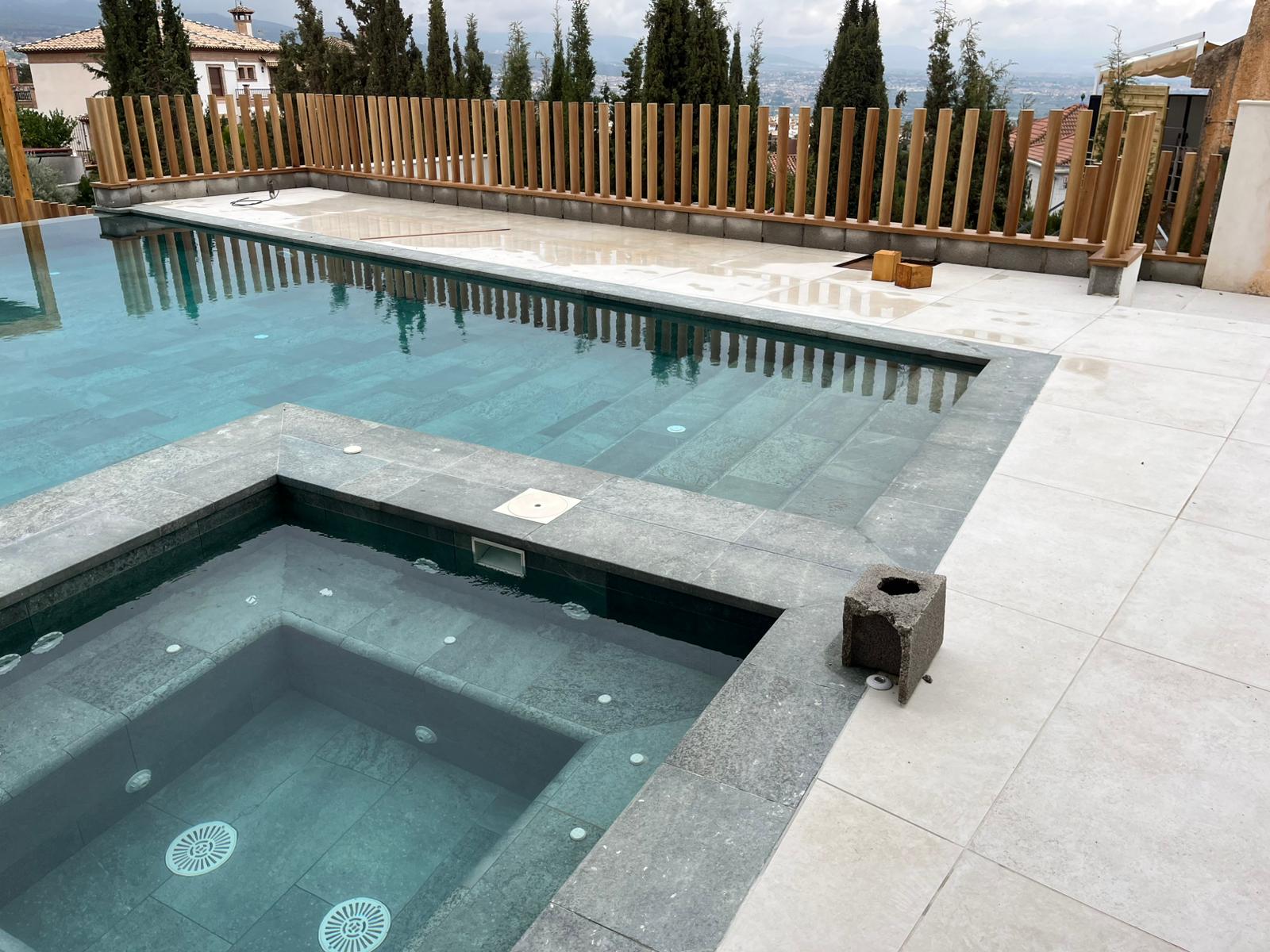Zona de piscina con piedra oscura y valla de madera